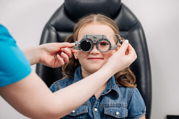 A female doctor holds special glasses to a patient for eye examination and lens selection in the...