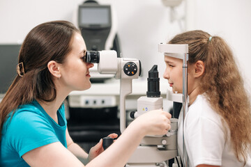 Close-up portrait of a happy little girl sitting in an optometrist's office while the doctor examines her eyesight in a modern clinic.