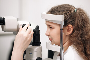 An ophthalmologist does an eye examination, working in a modern clinic with professional equipment. A girl checks a child's eyesight.