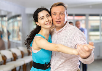 Portrait of positive adult pairs of different ages enjoying tango in modern dance hall together