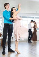 Fototapeta premium During rehearsal of reporting concert, guy and girl participants of dance workshop perform figure waltz. Several couples practice and hone their skills in performing waltz, classic slow dance style.