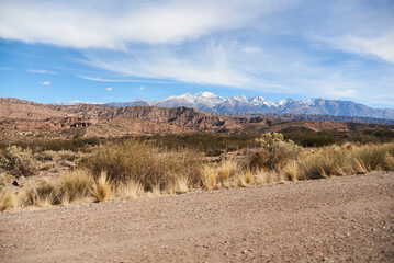 On the side of a gravel road in Mendoza, Argentina, a landscape stretches out with the mountains of...