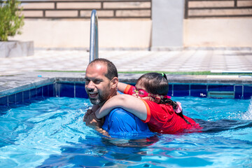 A cheerful father and son are having a great time in the water under the shining sun, smiling as they teach swimming. They look at the camera, capturing a real-life moment that strengthens their bond