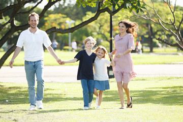 Fototapeta premium Happy family relaxing together at the park, caucasian family with father, mother, and children walking at the park.