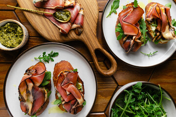 Appetizer toasts with prosciutto, pesto sauce, cheese and arugula on a table on a table
