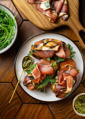 Appetizer toasts with prosciutto, pesto sauce, cheese and arugula