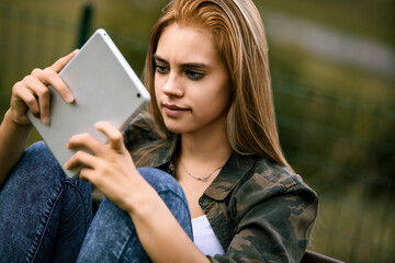Obraz premium Young woman browsing on tablet outdoors in thought