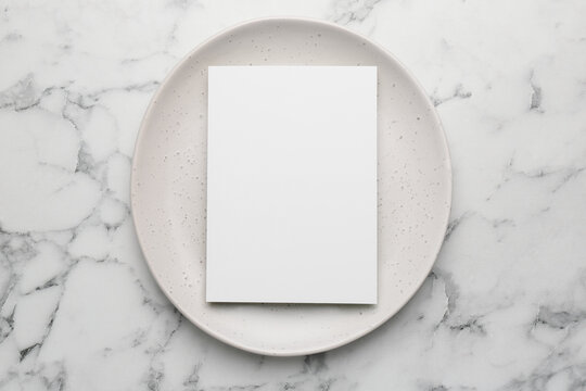 Empty menu and plate on white marble table, top view. Mockup for design
