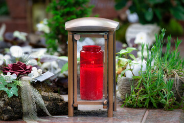 modern metal grave lantern with  burning devotional candle on a grave with tasteful decorations