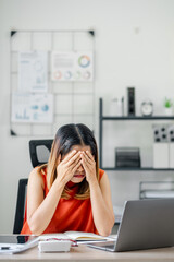 Businesswoman feeling stressed at her desk, hands on face, in a modern office setting with a laptop...