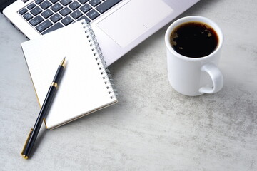 机にノートパソコンやノートを広げ、コーヒーを飲みながらデスクワークをしているイメージ
