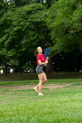 Smiling pretty happy woman holding yoga mat and water bottle barefoot in a public park outdoors. Yoga session and meditation concept