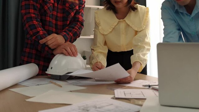 Architect and safety engineer discussion about building blueprint displaying on laptop on table with architectural document and wooden block scatter around at modern office. Closeup. Delineation.