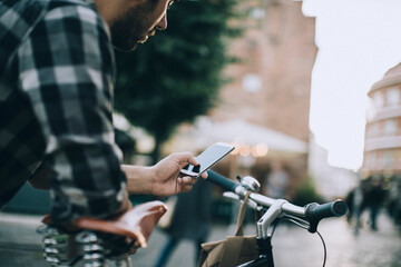 Man using smartphone while riding bicycle in city