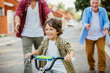 Obraz premium Father and grandfather teaching young boy to ride a bike on residential street