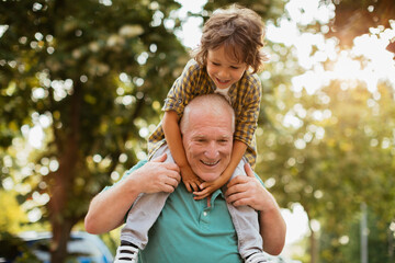 Grandfather giving piggyback ride to grandson in sunny park