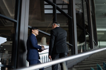 Two men in suits stood on the stairs. with one person holding a tablet They are discussing important matters.