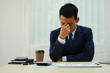 stressed businessman is sitting at his office desk, looking worried while working on his laptop....