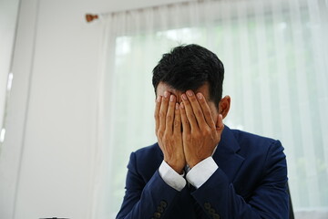 stressed businessman is sitting at his office desk, looking worried while working on his laptop. Overworked and frustrated, he faces financial problems and job pressures in his corporate banking role