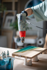 Female artist using dryer to disperse epoxy resin over canvas to create pattern of sea ocean waves. Woman hand palm art holding, working with tool to create artwork painting from fluid liquid.