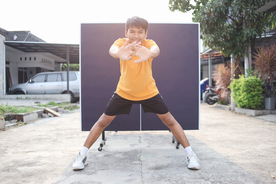 Friendly Young Asian Male Stretching Pushing Arms To The Front Against Ping Pong Table Background