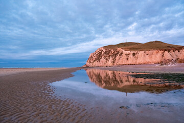 Stunning coastal cliffs reflected in tidal pools during dusk, showcasing natural beauty and tranquility.