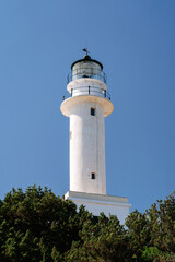 Tall white lighthouse, with a clear blue sky backdrop, symbolizing guidance, safety, and navigation for ships at sea.