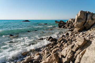 Serenity on a sunny day: pristine rocky shoreline meets the turquoise sea under a clear blue sky.