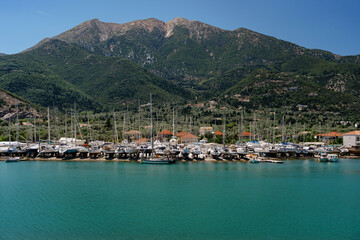 Fototapeta premium A tranquil marina filled with yachts, clear blue water, against a backdrop of lush green mountains under a bright sky.