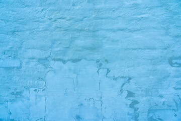 Old brick wall covered with plaster and blue paint. Uneven brick paint and traces of repair are visible. Background. Texture.