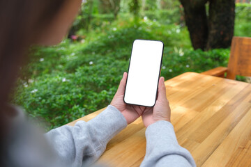 Mockup image of a woman holding mobile phone with blank white desktop screen in the outdoors