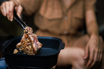close up  young asian woman sitting grilled meat in pan  picnic gas in the night camping.