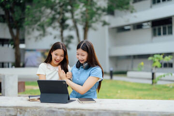 Two Happy Female Students Using Laptop Outdoors on Campus, Celebrating Success and Smiling