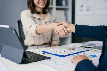Business Professionals Shaking Hands in Office Setting with Documents and Laptop on Desk