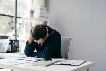Businessman Stressed at Work Desk in Modern Office with Documents and Laptop