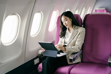 Businesswoman Working on Tablet During Flight in Airplane with Purple Seats and Natural Light