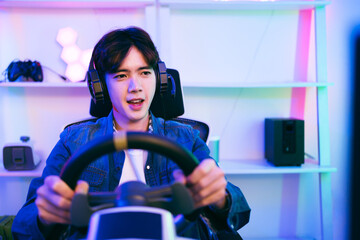 Asian male pro gamer playing an online car drive simulation game with steering wheel controller....