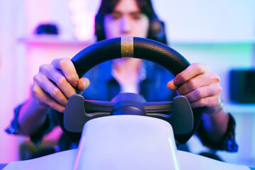 Asian male pro gamer playing an online car drive simulation game with steering wheel controller. Gamer winning an esports game with victory emotion. The player rejoices in victory in the competition. © artitwpd