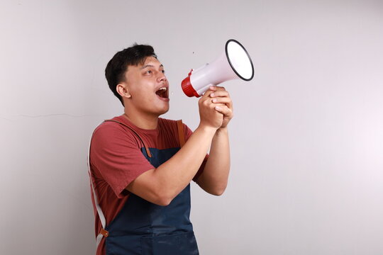 Young asian man barista barman employee wear blue apron work in coffee shop standing while holding a megaphone