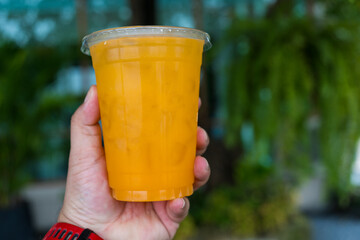 Orange juice ice in plastic cup. Healthy orange juice detox green nature background