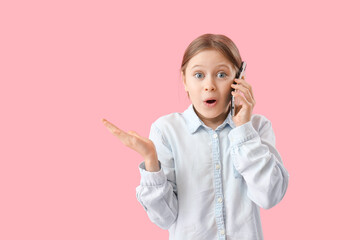 Shocked little girl talking by mobile phone on pink background