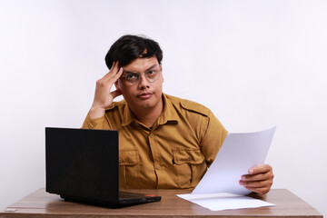 Stressed male teacher in civil servant uniform with paper and laptop on the desk holding a paper