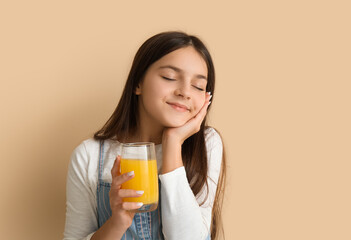 Little girl with glass of orange juice on beige background