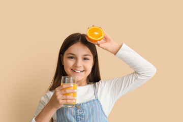 Little girl with glass of juice and orange on beige background