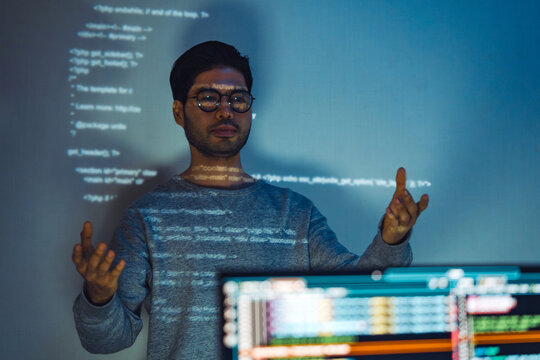 Indian man programmer standing in front of a screen with code projected  presentation the integration of technology and human expertise in software development