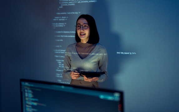 asian woman programmer standing in front of a screen with code projected  presentation the integration of technology and human expertise in software development