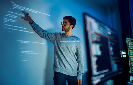 Indian man programmer standing in front of a screen with code projected  presentation the integration of technology and human expertise in software development - Powered by Adobe