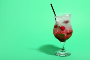 Glass of fresh raspberry mojito on green background