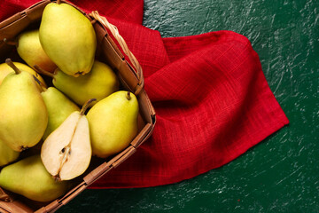 Wicker basket with fresh pears on green background