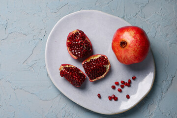 Plate with fresh pomegranates and seeds on blue background